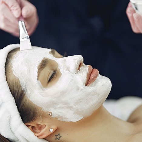 A woman on her back having a thick, white serum applied to her face in a spa